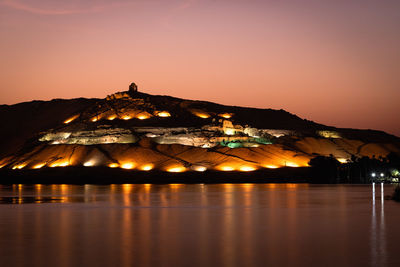 Illuminated town by lake against sky at night