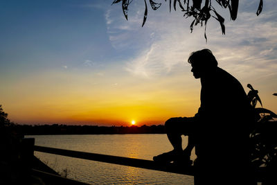 Silhouette man standing by lake against sky during sunset