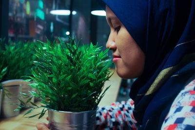 Side view of young woman smelling plant on table