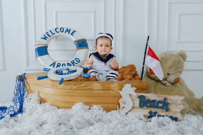 
the baby boy was wearing a white and blue sailor outfit, complete with a red and white flag.