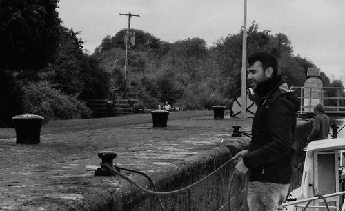 Young man standing by trees against sky
