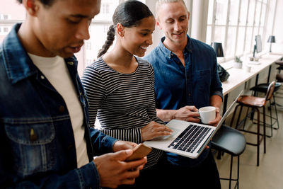 Smiling businesswoman discussing with colleagues over laptop in office