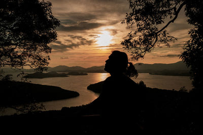 Silhouette woman looking at lake against sky during sunset