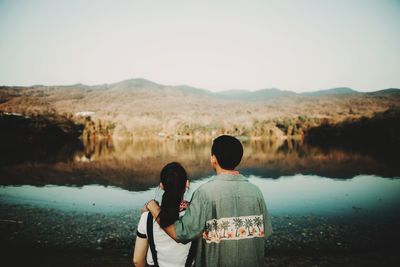 Rear view of friends standing on lake against clear sky