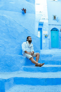 Full length of man sitting on retaining blue wall in town