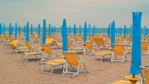 Empty chairs and tables on beach against sky