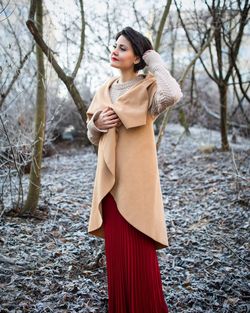 Woman in long dress standing against trees on field during winter