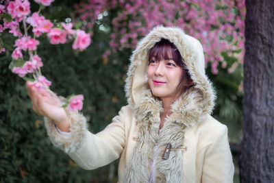 Smiling woman touching flowers while standing outdoors