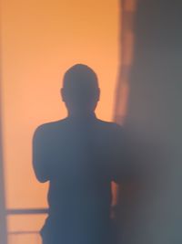 Rear view of silhouette man standing against orange sky