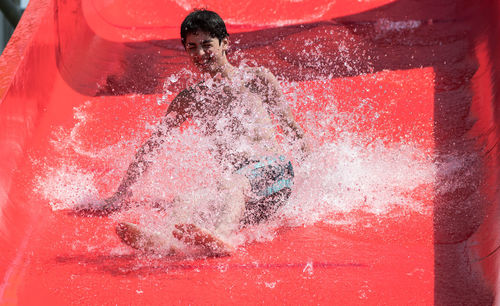 Low angle view of teenage boy sliding on red water slide