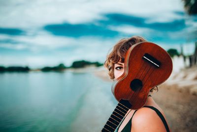 Side view portrait of young woman with ukulele at lakeshore
