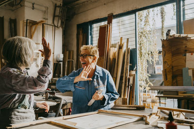 Happy senior craftswomen giving high-five at carpentry workshop