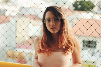 Portrait of beautiful young woman against fence