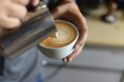 Midsection of person pouring milk in coffee