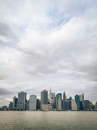 View of new york city skyline from brooklyn pier park buildings in city against cloudy sky