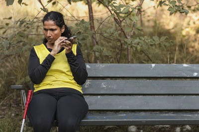 Visually impaired woman sitting on bench and using cell phone