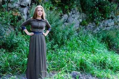 Portrait of young woman in dress standing against rock formation