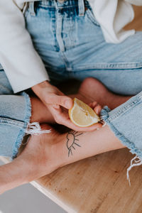 From above of crop anonymous female sitting on wooden table with slice of fresh ripe lemon and showing concept of healthy food and diet