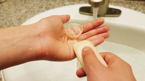 Cropped hands washing condom with soap at sink