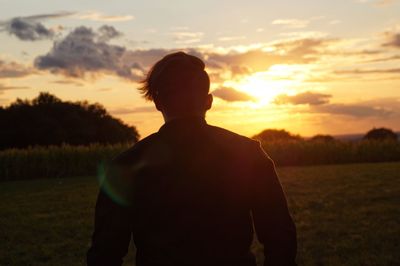 Rear view of man standing on field against sky during sunset