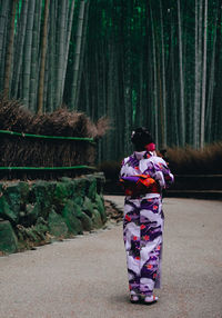 Rear view of woman standing on footpath against trees