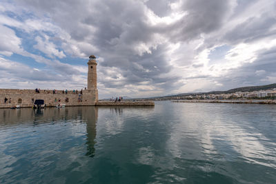 Lighthouse on sea by buildings against sky