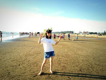 Full length portrait of smiling girl standing at beach against sky