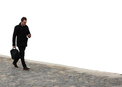 Full length of man walking by white wall on sidewalk