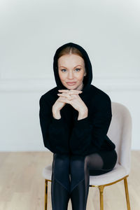 Portrait of woman sitting on chair against wall