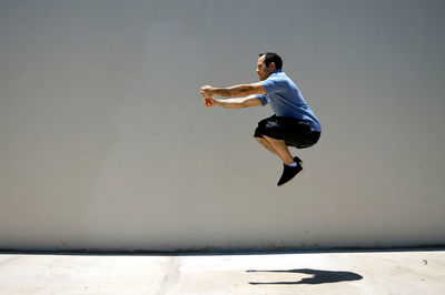 Side view of man levitating over sidewalk by wall