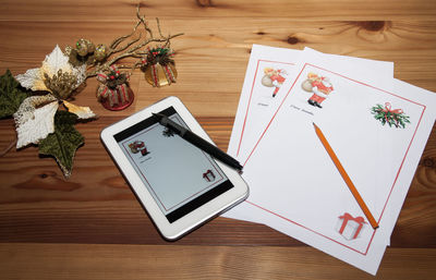 High angle view of digital tablet with christmas greeting cards on table