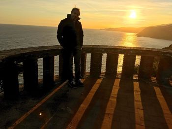 Rear view of silhouette man on beach against sky during sunset