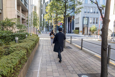 Rear view of man walking on footpath amidst buildings