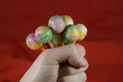 Cropped hand holding colorful lollipop against red fabric