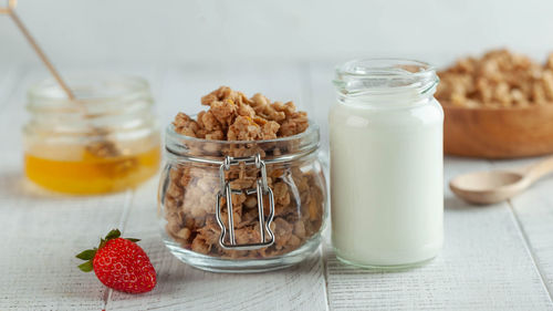 Banner with homemade granola, milk in a jar, honey and strawberries on a wooden background. 