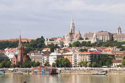 Sailboats in river by buildings in city against sky