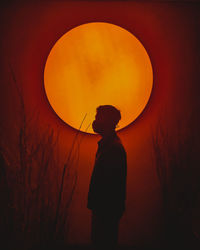 Rear view of silhouette man standing against orange sky