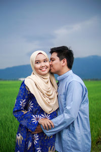 Happy young couple standing against sky