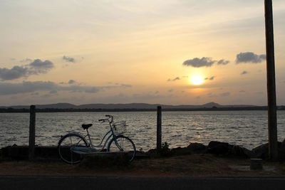 Bicycle on beach against sky during sunset
