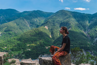 Young woman sitting on mountain against sky