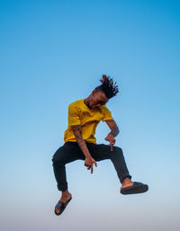 Full length of man jumping against clear blue sky