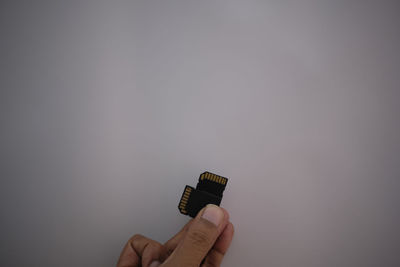 Cropped hand of person holding memory card camera against gray background