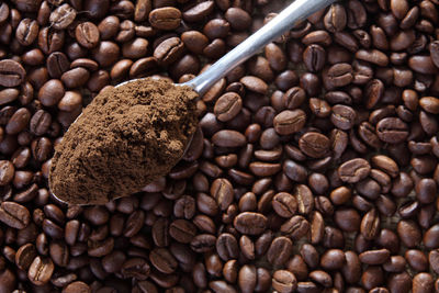 High angle view of ground coffee in spoon on roasted beans