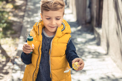 Smiling boy with bubble wand standing on footpath during sunny day