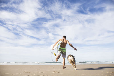 Man carrying surfboard running with dog on the beach