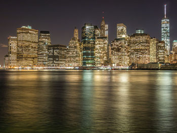 Illuminated buildings by river against sky at night