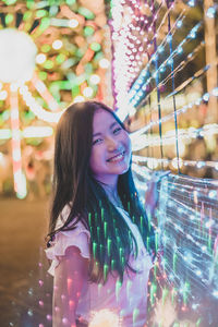 Digital composite portrait of smiling young woman standing at amusement park during night