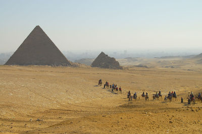 People riding horses in desert against clear sky