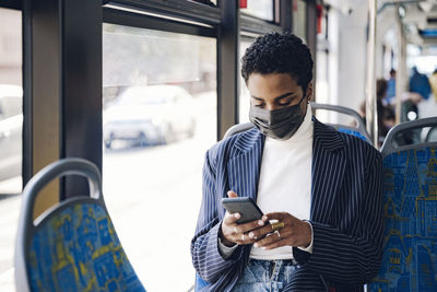 Young businesswoman using mobile phone in bus during covid-19