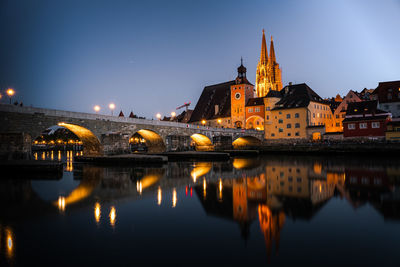 Illuminated buildings by river against sky at night